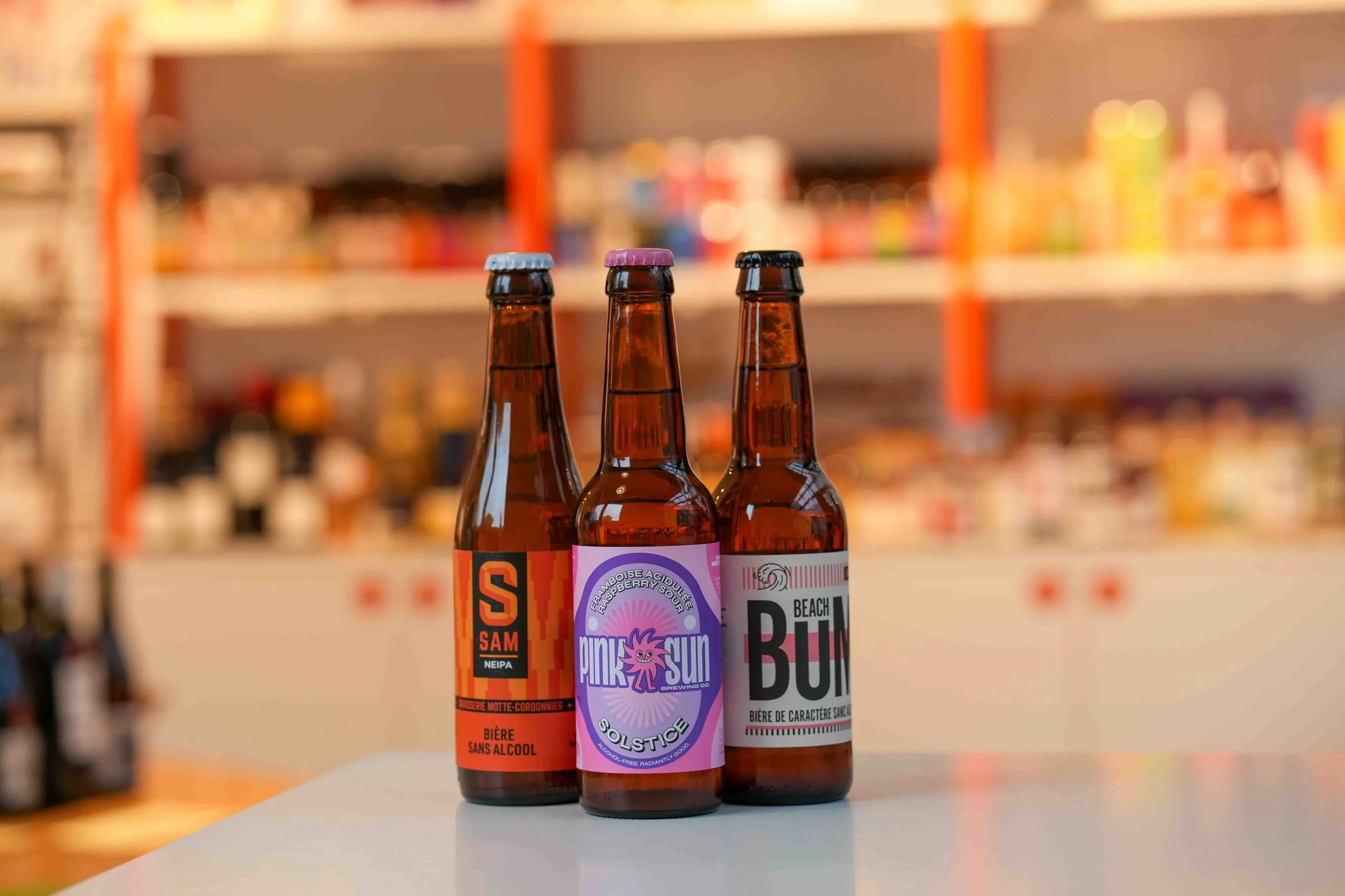 Trois bières sans alcool sur le comptoir de la cave : la NEIPA Sam, la Pink Sun Solstice à la framboise et la Beach Bum