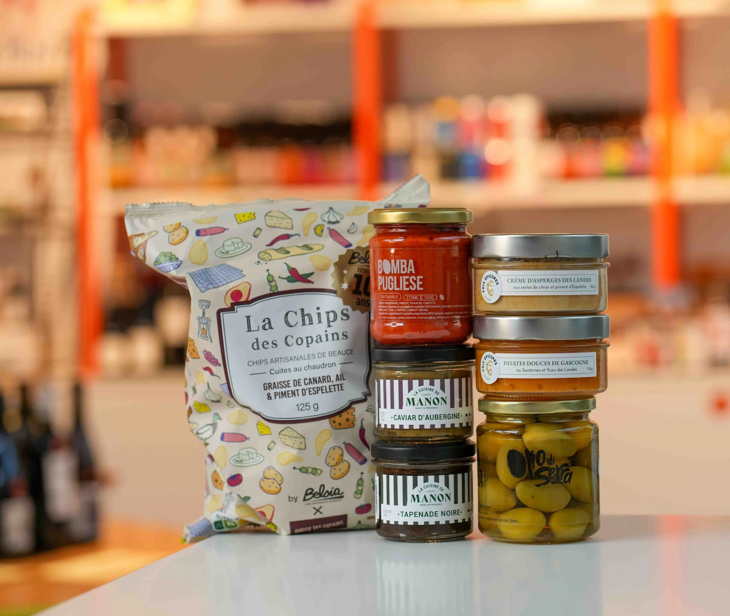 Épicerie fine sur le comptoir de la cave : la Chips des Copains, la Bomba Pugliese, le caviar d'aubergine et la tapenade de La Cuisine de Manon, des crèmes d'asperges et de patates douces, des olives