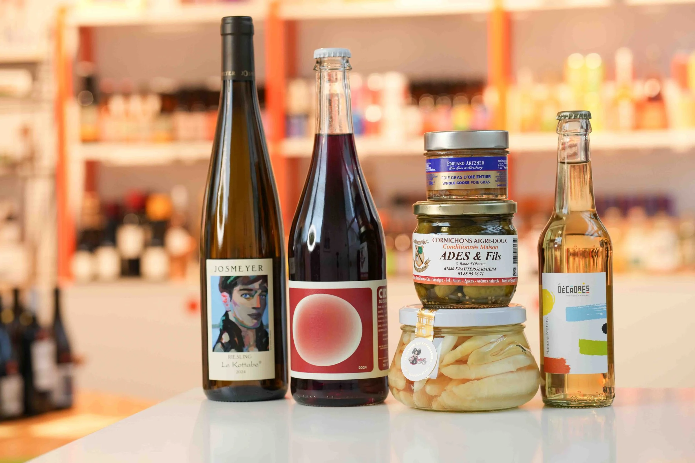 Produits d'Alsace sur le comptoir de la cave : riesling Josmeyer Le Kottabe, cidre, foie gras d'oie Édouard Artzner, cornichons Ades & Fils et un bocal d'asperges