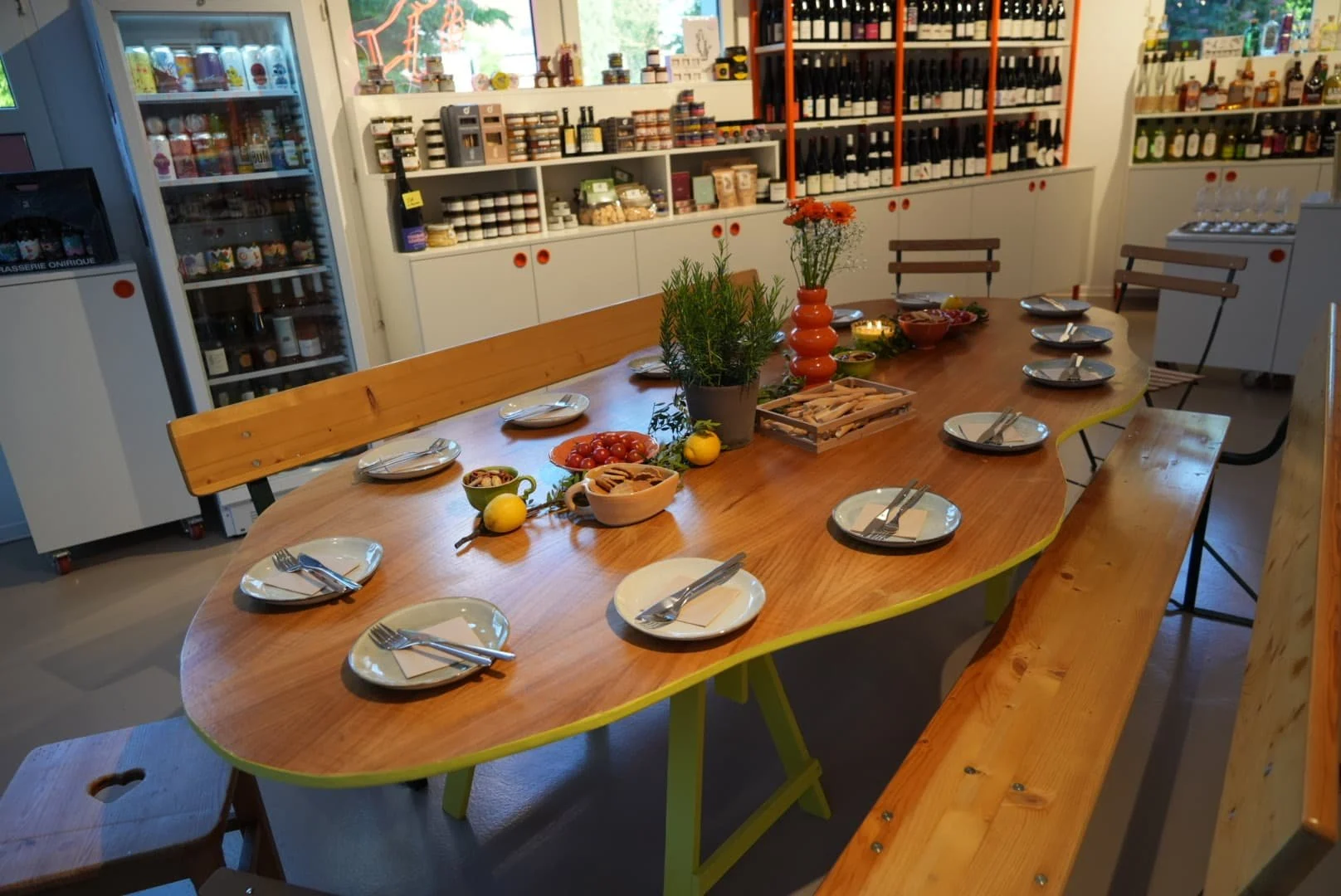 Table ovale en bois aux pieds jaunes dressée pour une dégustation dans la cave, devant les frigos et les étagères