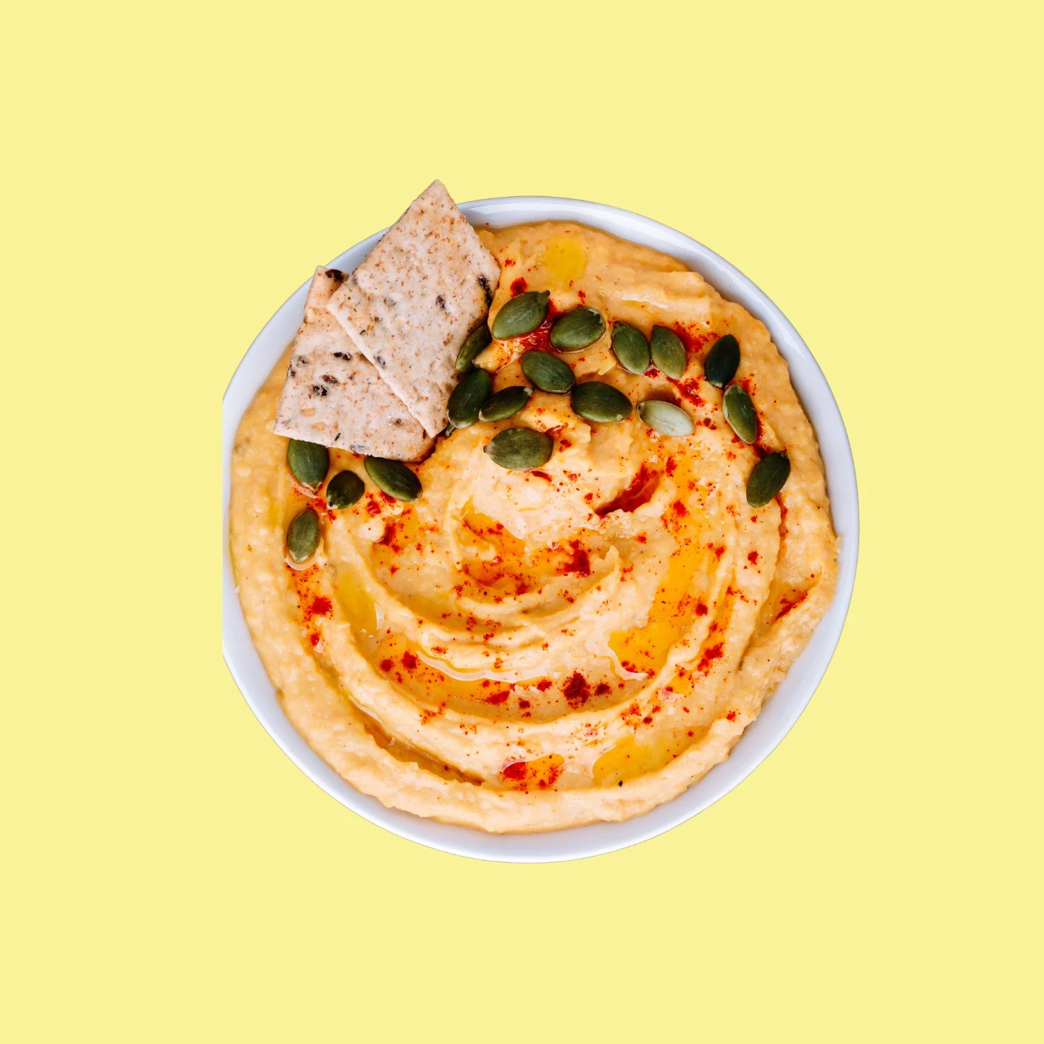 Un bol de dip de potimarron et féta au paprika, garni de graines de courge et d'un cracker, sur fond jaune